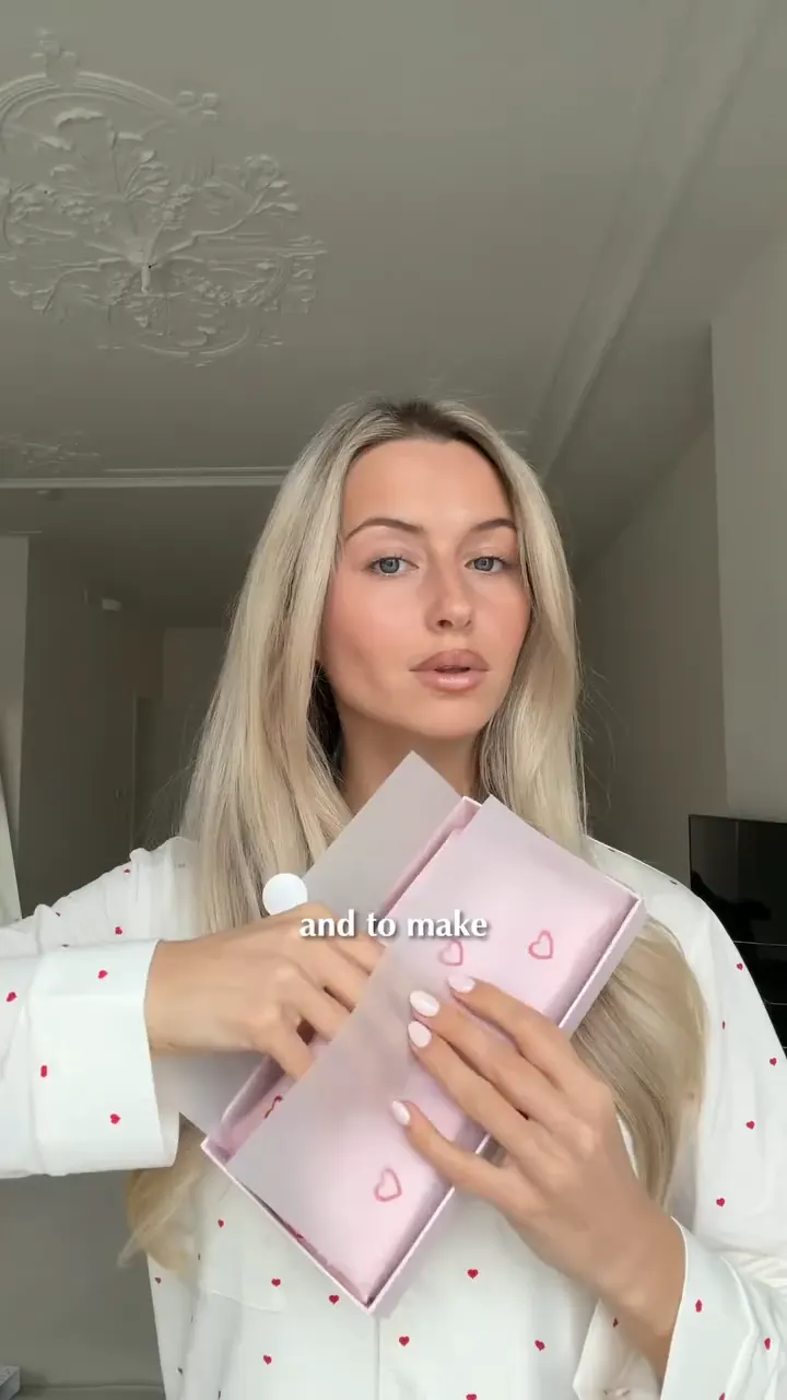 A creator in heart-print pajamas opening a pale pink gift box.